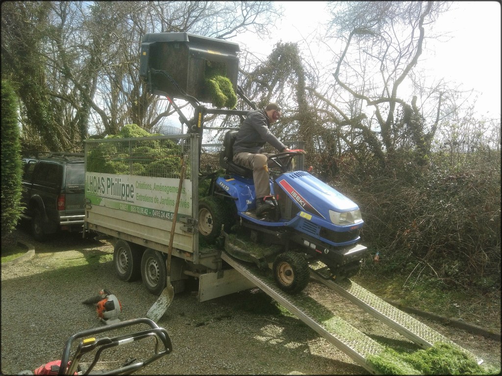 Un tracteur tondeuse vide son bac à pelouses dans une remorque