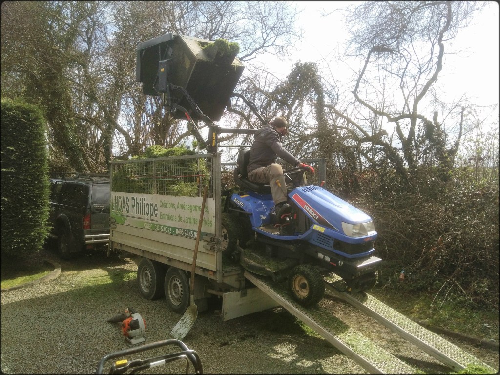 Un tracteur tondeuse vide son bac à pelouses dans une remorque