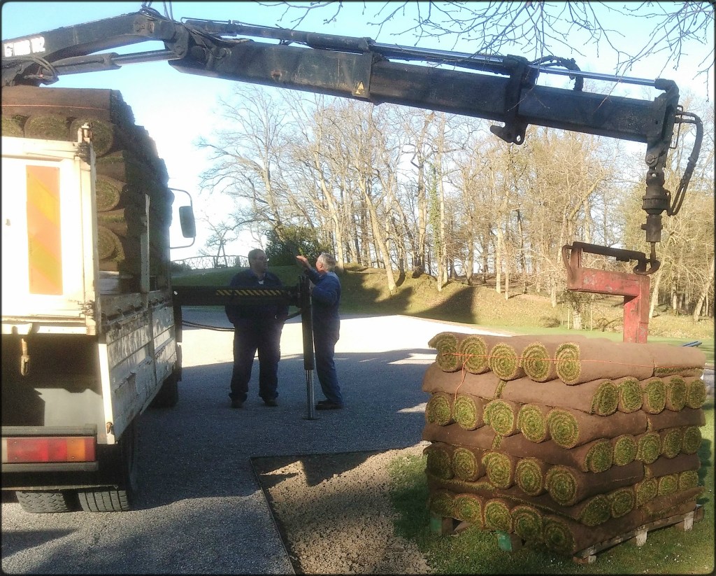 un camion grue décharge des palettes de rouleaux de gazons
